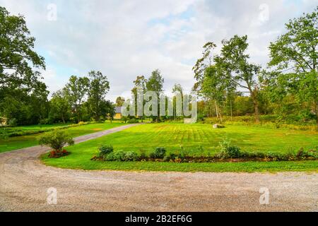 Una strada sterrata rurale corre lungo un giardino curato e prato vicino a una casa isolata gialla nella campagna della Finlandia. Foto Stock