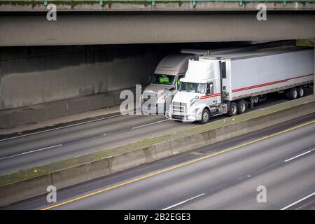 Due diversi semi-camion per grandi carri di tipo industriale con motori diesel e semi-rimorchi per frigoriferi che trasportano carichi commerciali in funzione sul div Foto Stock