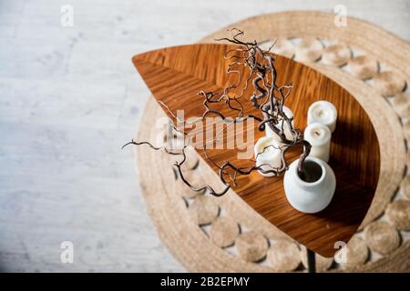 Piccolo tavolo in legno con vaso in ceramica con rami su un tappeto di paglia rotonda. Interno boho. Ambiente naturale decor.Hygge stile scandinavo concept.COZY Foto Stock