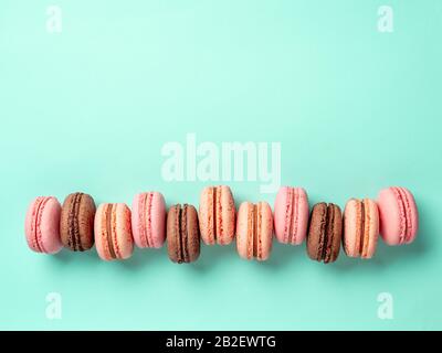 Macarons con spazio di copia. Fila di macaron francesi perfetti o macaron su sfondo blu turchese. Vista dall'alto o piatto Foto Stock