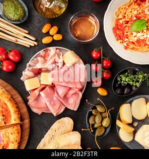 Cibo italiano, top shot su sfondo nero. Antipasti, spaghetti, formaggio, prosciutto, capperi, vino, olive, pomodori, sparati dalla cima su nero Foto Stock
