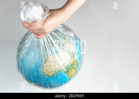 La mano umana tiene la terra in cattività. Globo in un sacchetto di plastica bianco. Il concetto di disastro ambientale su un fondo bianco isolato Foto Stock