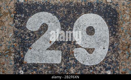 Weathered and faded number twenty nine painted on a rough concrete surface image in horizontal format with copy space Foto Stock