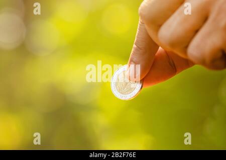 Primo piano tenere la moneta tailandese 10 Baht su sfondo verde natura sfocata. Concetto di risparmio economico Foto Stock