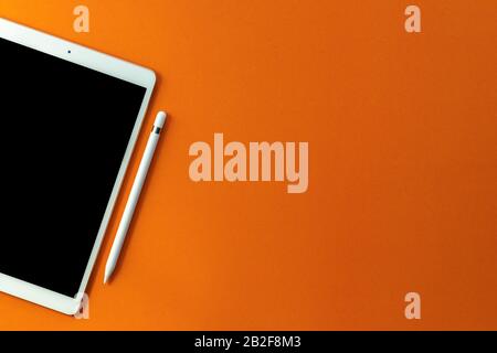 In alto nuovo modello di tablet con schermo nero e matita su sfondo arancione. Copiare lo spazio per il testo o il disegno Foto Stock