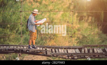 Turista asiatico che cammina sul ponte di legno vecchio e rotto. Rischi del concetto di viaggio Foto Stock