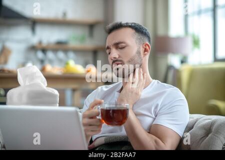 Giovane uomo dai capelli scuri che ha una gola irritata Foto Stock