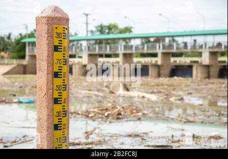 Numero giallo di indicatore del livello dell'acqua sul palo alla diga. Sfocatura backgrounf della diga in Thailandia Foto Stock