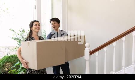Vista frontale di una felice coppia caucasica che si sposta nella loro nuova casa arrivando nel corridoio che porta scatole di cartone e sorridente Foto Stock