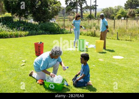 Vista ad alto angolo di una donna afroamericana e di un giovane ragazzo inginocchiato in un campo indossando guanti e t-shirt con volontario scritto su di loro, filli Foto Stock