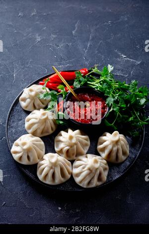 Khinkali, gnocchi con ripieno di carne servito su un piatto nero con jadika e coriandolo fresco, cucina georgiana, vista verticale dall'alto Foto Stock