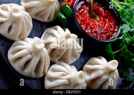 Primo piano di Khinkali, gnocchi con ripieno di carne servito su un piatto nero con jadika e coriandolo fresco, cucina georgiana, vista orizzontale dall'alto Foto Stock