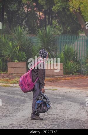 Alberton, Sud Africa - un uomo nero senza casa inidentificato con i suoi effetti personali isolato su una strada pubblica in una noiosa mattina d'autunno Foto Stock