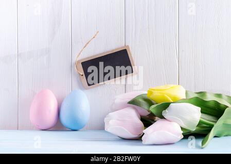 Buono Pasqua dalle uova dipinte a mano, lavagna per messaggi e tulipani freschi su sfondo di legno grigio chiaro. Foto Stock