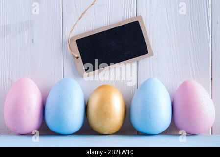 Chiudi la cartolina di invito di Pasqua con uova colorate dipinte a mano e lavagna per messaggi su sfondo di legno grigio chiaro. Foto Stock