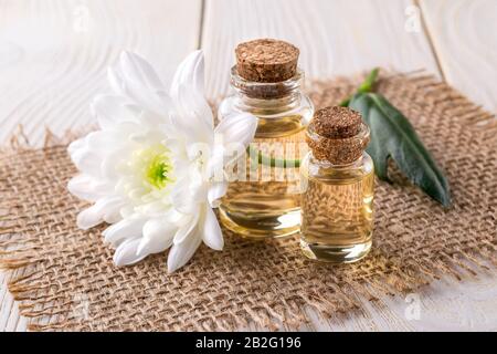 Due bottiglie di vetro di olio essenziale di crisantemo e fiore bianco di crisantemo su uno sfondo di iuta. Spa, bellezza, cura della pelle e cosmetologia concetto. Foto Stock