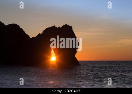 Sole che sorge attraverso l'arco calcareo naturale di Durdle Door, solstizio d'inverno, Dorset, Inghilterra, Regno Unito Foto Stock