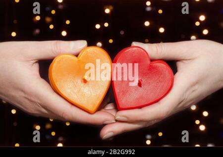 Due candele a forma di cuore in mani femminili su uno sfondo di bokeh Foto Stock