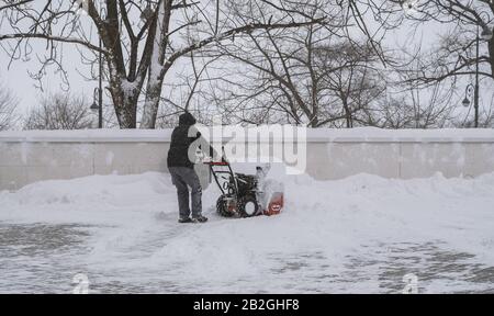 Uomo con un soffiatore di neve che rimuove la neve sulla strada. Foto Stock