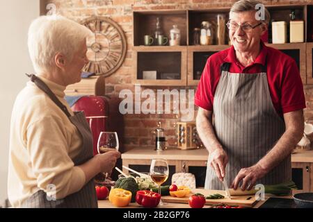 Romantica coppia anziana bere vino e preparare la cena insieme in cucina Foto Stock