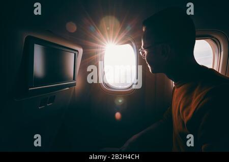 Viaggia in aereo durante la giornata di sole. Giovane uomo con occhiali che guarda attraverso la finestra. Foto Stock