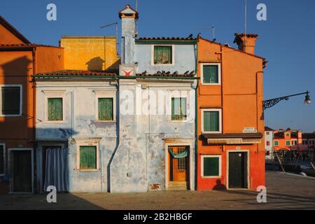 Burano, Venezia, finestre colorate con persiane verdi in case blu e arancioni, un mosaico di architettura, forma e forme alla luce del mattino presto Foto Stock