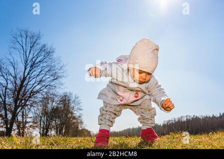 Bambino che indossa caldo berretto, felpa e stivali rossi all'aperto in zona rurale alla scoperta della natura in primavera, giornata di sole. Foto Stock