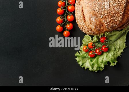 Composizione piatta con pomodori ciliegini, lattuga e pane su sfondo nero e luogo per il testo. Ingredienti per preparare un sandwich vegetariano. Foto Stock