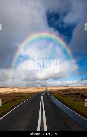 Un arcobaleno su una strada rurale flessibile autostrada in llangynidr Galles del sud Foto Stock