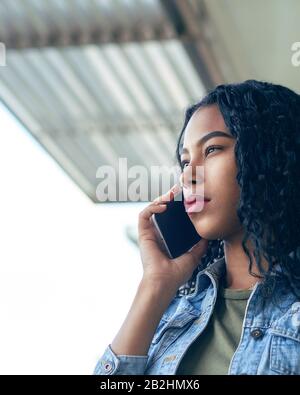 Una donna latina concentrata con capelli ricci che ha una chiamata telefonica Foto Stock