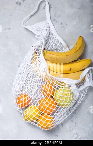 Borsa a corda con frutta mista: Banane, limoni, mele, arance. Concetto di zero sprechi. Sfondo grigio, spazio di copia, primo piano. Vista dall'alto. Foto Stock