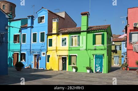 Blu, verde, giallo, colorate case a due e tre piani di Burano, Venezia in una giornata di sole. Tende su porte, finestre con copertura, camini Foto Stock
