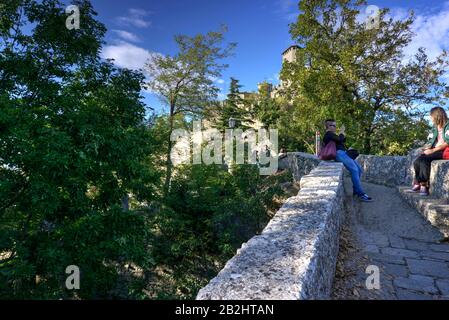 San Marino, San Marino - 19 ottobre 2019: Due turisti seduti e parlando su pareti di passerella in pietra con la Torre Guaita sullo sfondo. Foto Stock