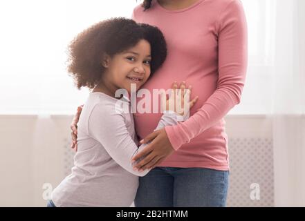 Primo piano di piccolo nero che abbracci il pancino di sua madre incinta Foto Stock