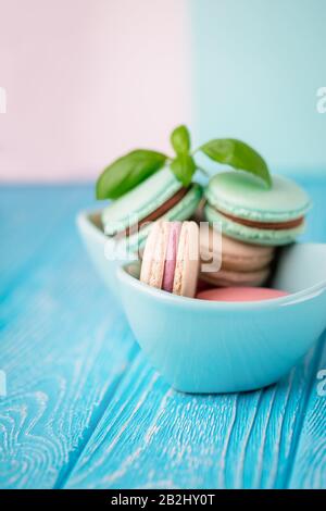 Ciotola turchese di macaroni colorati francesi o macarons su sfondo di legno turchese Foto Stock