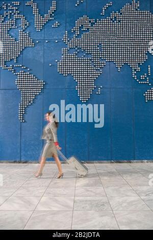 Donna d'affari con valigia che cammina oltre la mappa del mondo sul muro Foto Stock