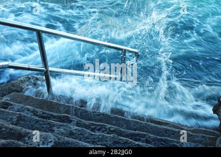 Spruzzi d'acqua bianca dell'oceano, schiume e picchi sui gradini e corrimano Dei Bagni Giles, piscina di roccia oceanica Coogee Bay, Sydney, Australia Foto Stock