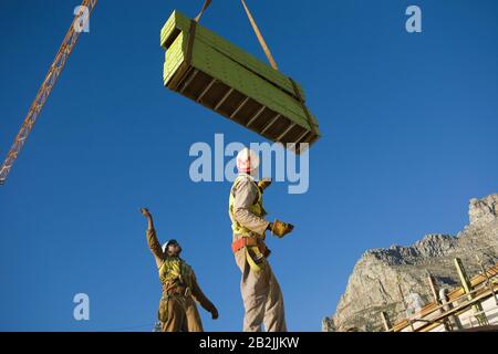 I lavoratori manovrano i materiali da costruzione sulla gru a torre Foto Stock
