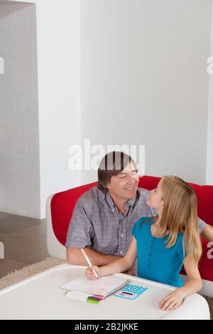 Padre e figlia che si guardano l'un l'altro mentre fanno i compiti insieme Foto Stock