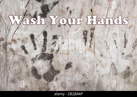 Primo piano di stampe a mano nere su pareti di cemento grunge con grafica di testo lavarsi Le Mani. Foto Stock