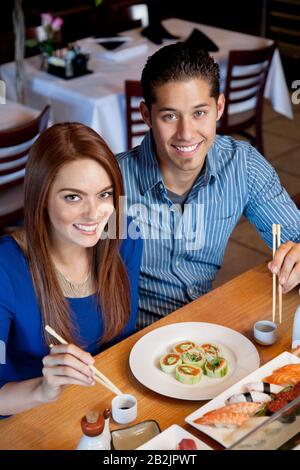 Ritratto di una coppia felice mangiare sushi con bastoni in ristorante giapponese Foto Stock