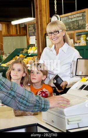 Ritratto di una donna anziana felice con i nipoti in piedi al banco di cassa nel mercato del coltivatore Foto Stock