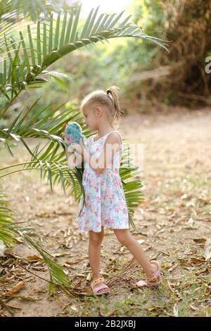 Bambina che gioca con il giocattolo e sta accanto alle foglie di palma. Foto Stock