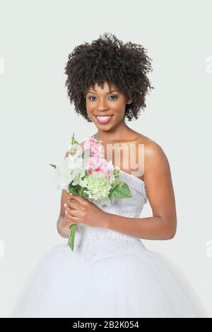 Ritratto di bella sposa afroamericana che tiene bouquet su sfondo grigio Foto Stock