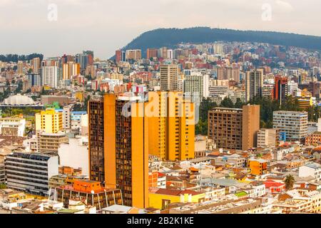 Una vista aerea di un'area urbana densamente costruita caratterizzata da un mix di alti e bassi edifici in vari colori, tra cui prominenti strutture arancioni e gialle. La città si estende verso un Foto Stock