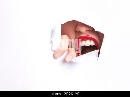 Primo piano di furiosa giovane donna con labbra rosse che cercano di liberarsi dalla parete di carta Foto Stock