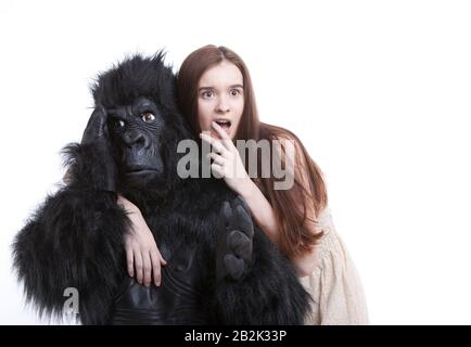 Donna giovane scioccata con l'uomo irritato in costume gorilla su sfondo bianco Foto Stock