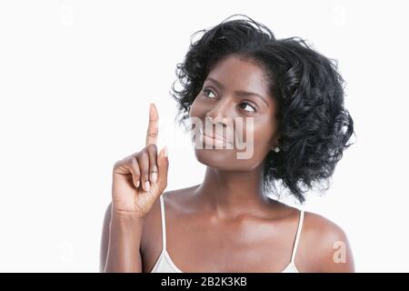 Giovane donna afroamericana che punta il dito indice verso l'alto su sfondo bianco Foto Stock