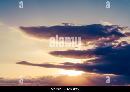 Alba, il sole splende forte dall'orizzonte su tutte le nuvole e sotto il cielo blu Foto Stock