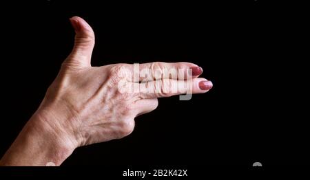 Mani di una donna anziana che fanno un gesto di scatto contro sfondo nero Foto Stock